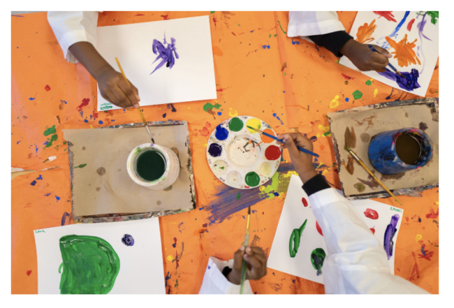 A few student hands playing in different art supplies photographed top down